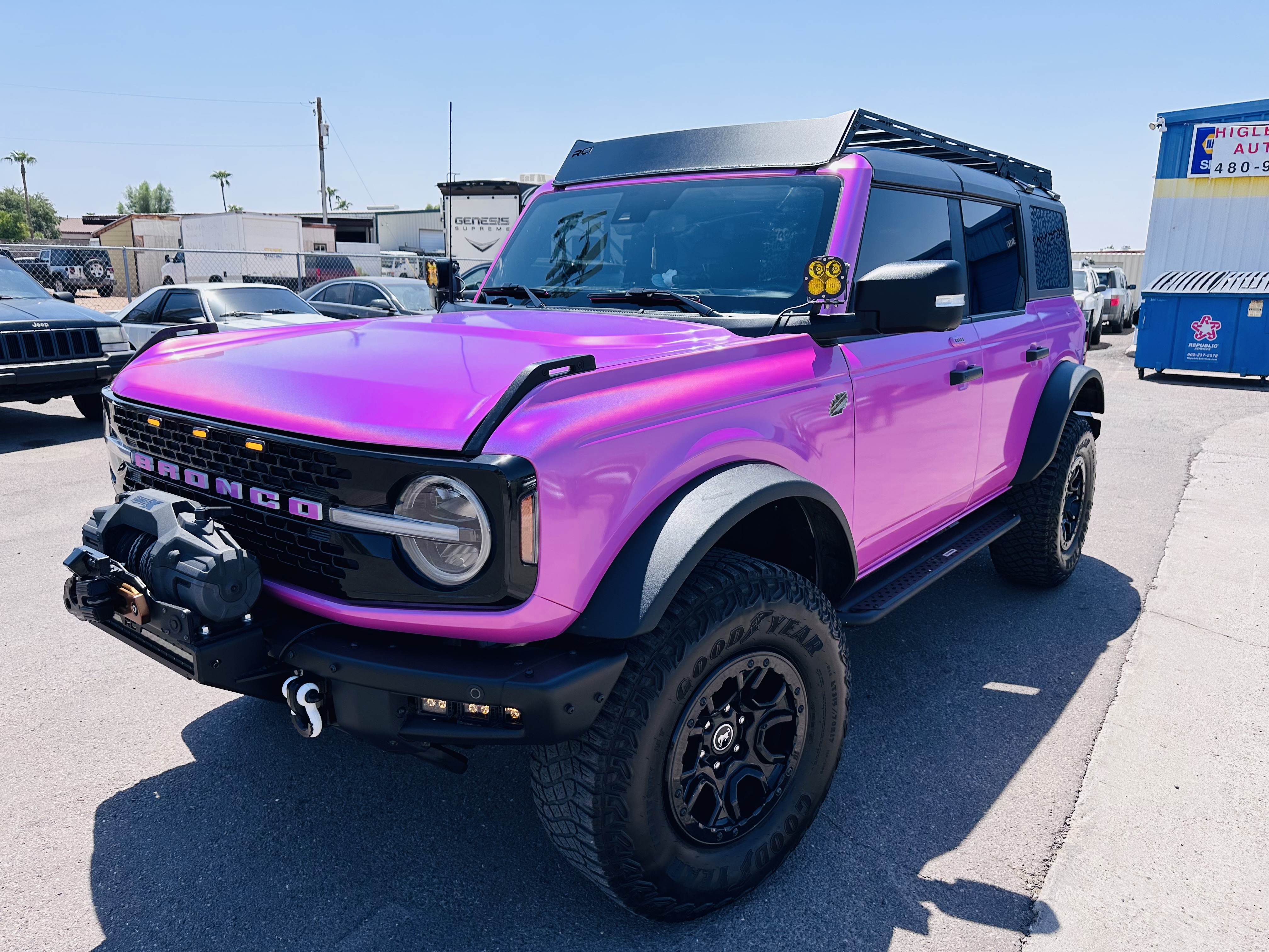 Bright purple Ford Bronco with off-road tires and roof rack outside an automotive workshop